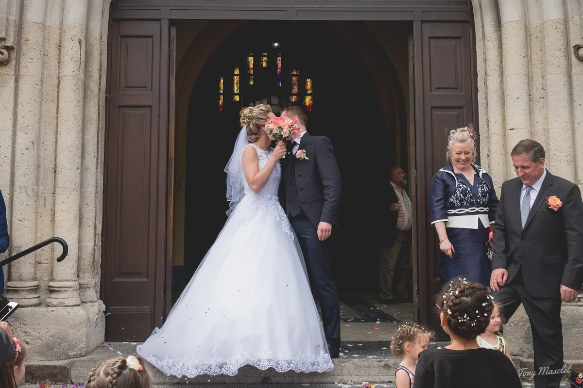 Photographe mariage Nieppe – baiser des mariés derrière le bouquet au porche de l'église