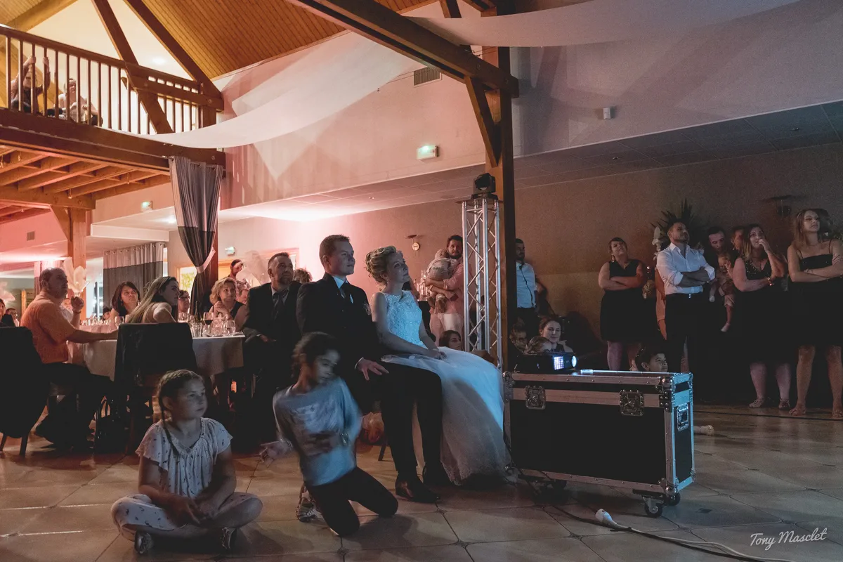 Photographe mariage Nieppe – les mariés regardent le diaporama sous la charpente en bois