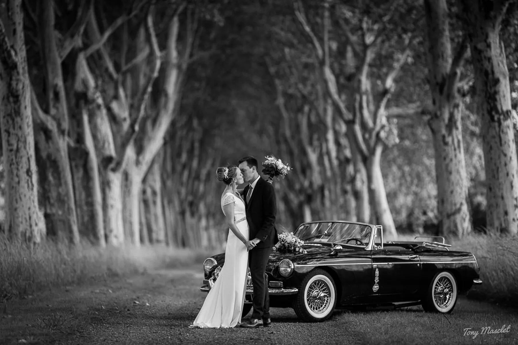 Séance de couple lors d'un mariage, allée d'arbres avec voiture ancienne, Tony Masclet photographe